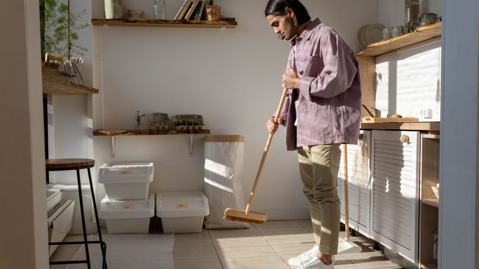 Someone sweeping a sunny kitchen next to stacked recycling bins