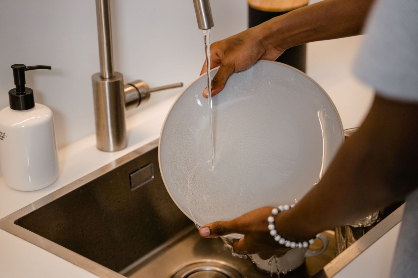 Someone rinsing a plate under the kitchen tap