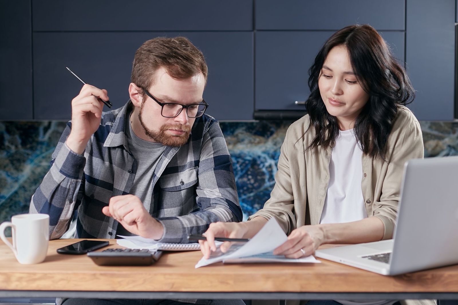 A couple at a kitchen table going over figures with a calculator and a laptop